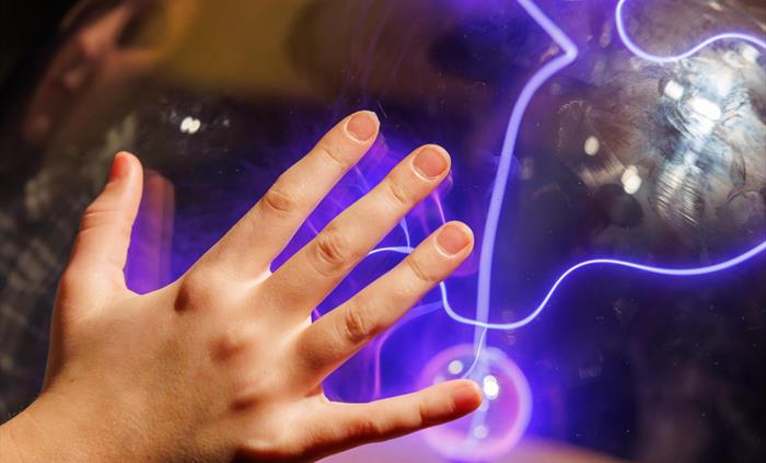 A child resting their hand on the case of the Plasma Sphere exhibit, attracting coils of electricity to their fingertips.